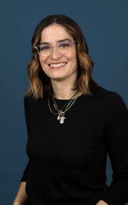 Woman wearing a black shirt and glasses standing against a blue background